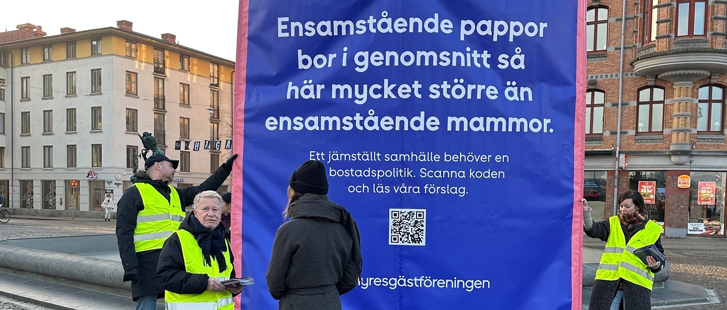 Personer på torg i Göteborg som håller i blått plakat med vit text om jämställdhet