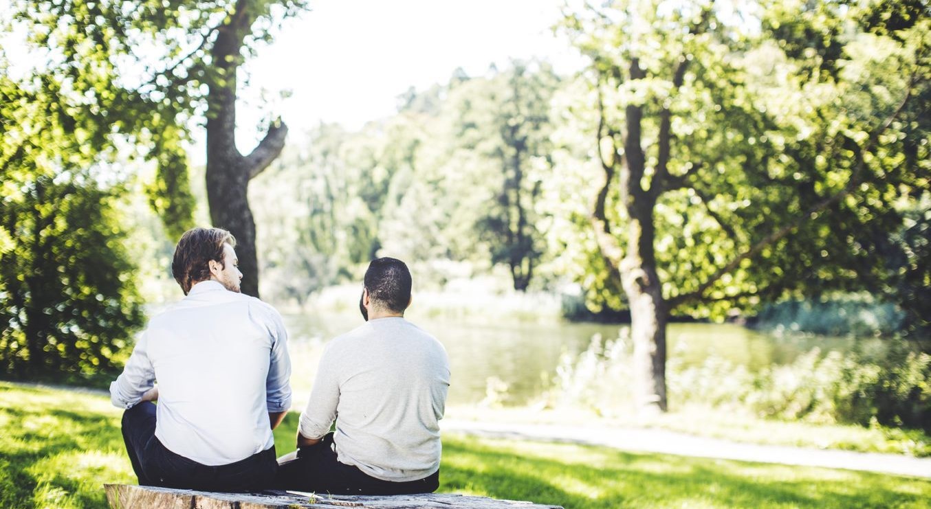 Bilden visar två personer som sitter vid en sjö.