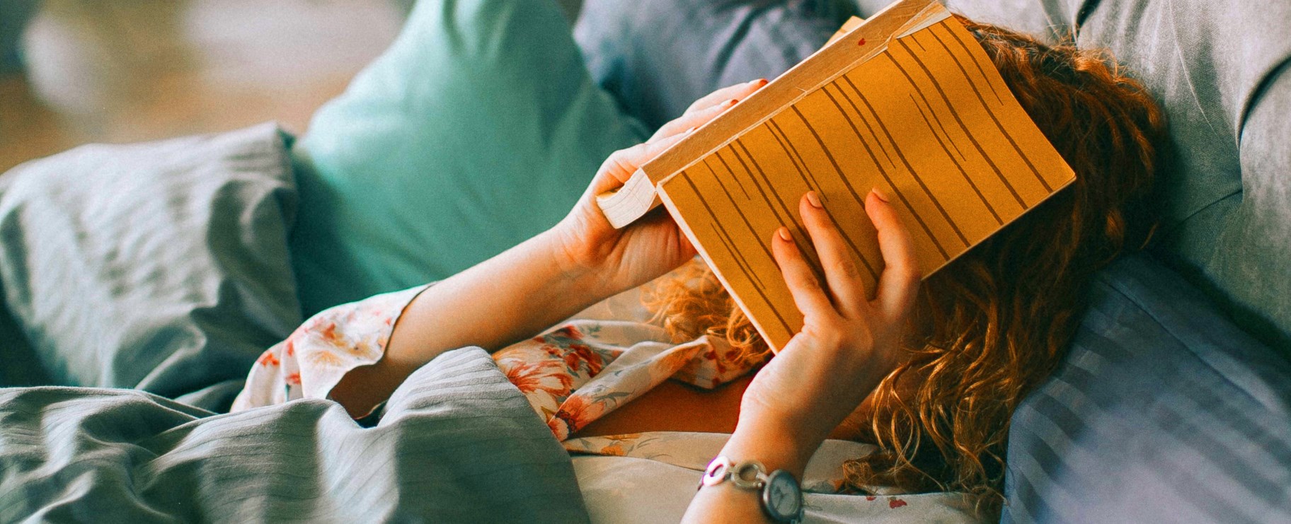 Bilden visar en person som ligger med en bok över ansiktet i en hotellsäng.