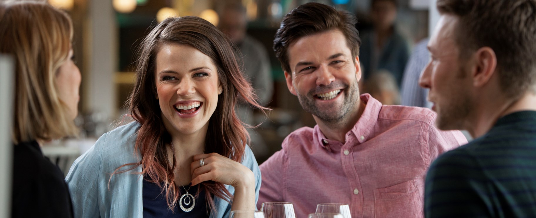 Bilden visar fyra personer skrattandes vid ett restaurangbord.