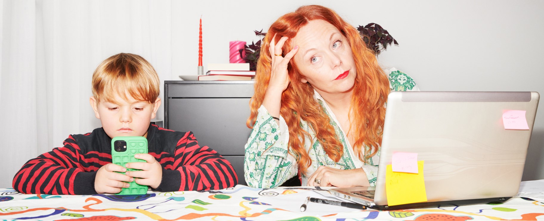 En mamma och hennes lilla son sitter vid ett bord framför datorn hemma i lägenheten