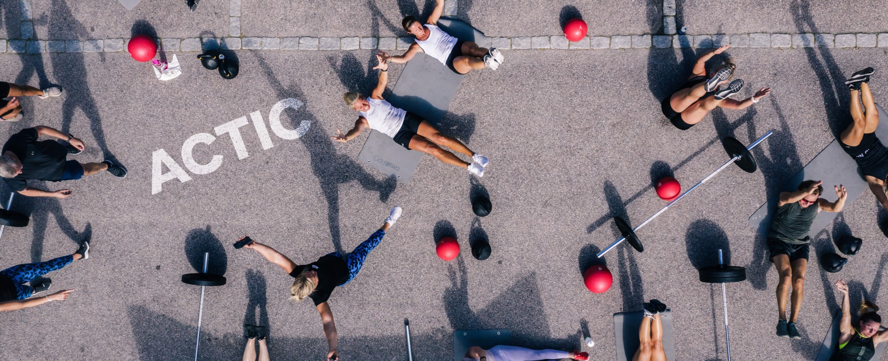 Bilden visa flera personer som tränar vid ett gruppträningspass hos Actic. BIlden är tagen uppifrån och Actics logotyp syns på marken.