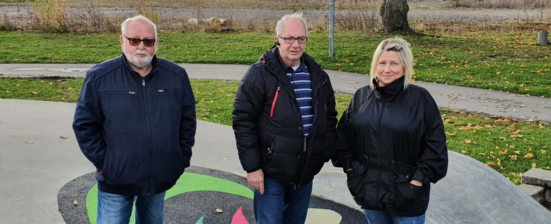 Tre personer står bredvid varandra i en park.