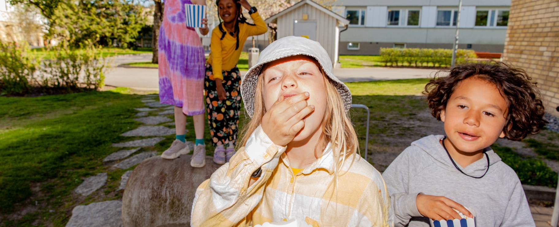 Två barn som är ute på gården och äter popcorn