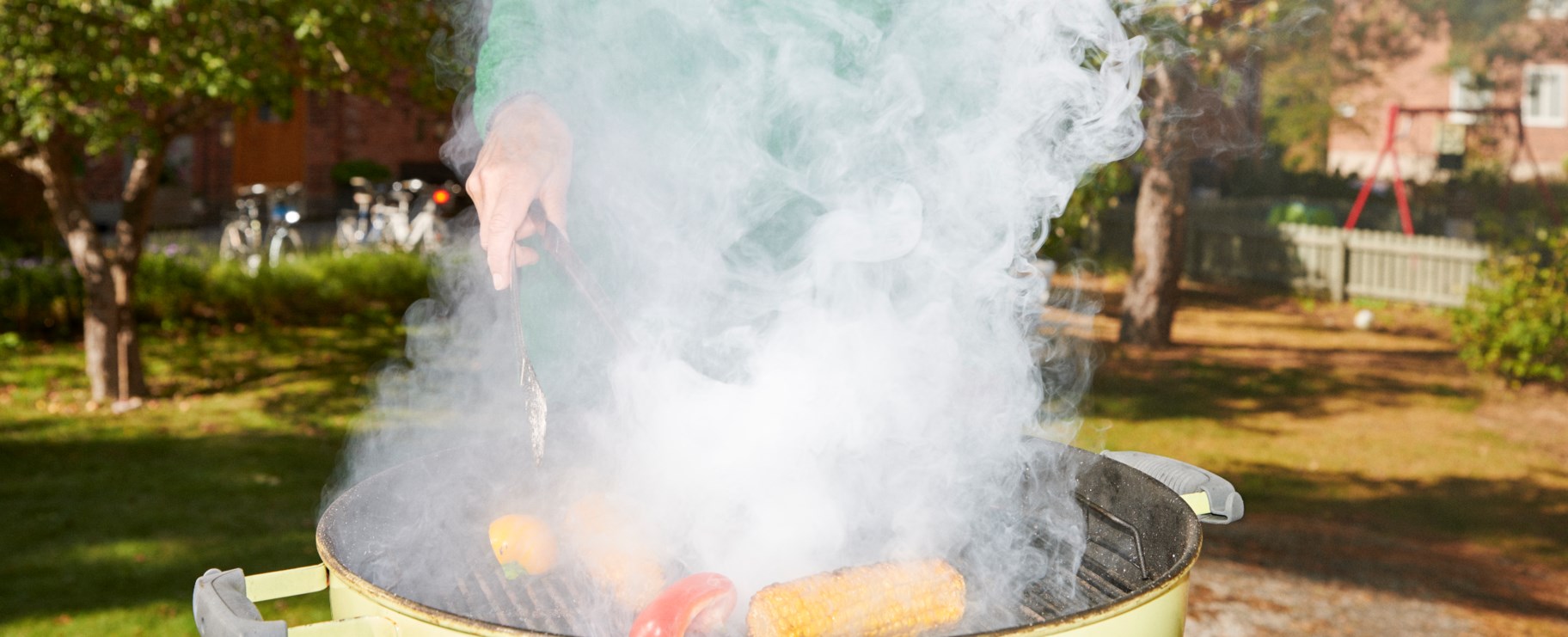 Kvinna står vid en grill som ryker utomhus på gården