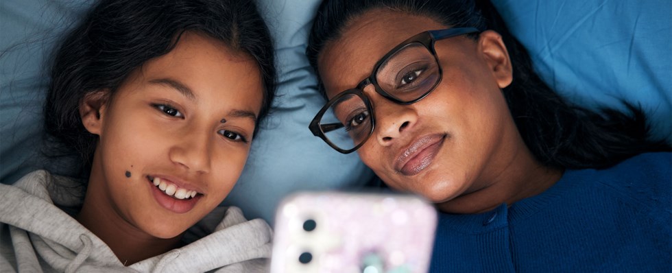 Tjej och kvinna ligger på kudde läser i mobil