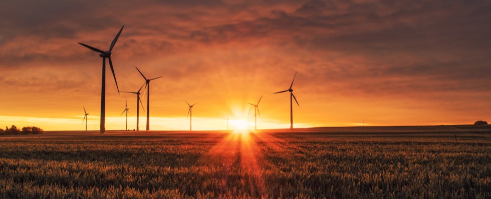 Några vindkraftverk som står på en äng i solnedgången.