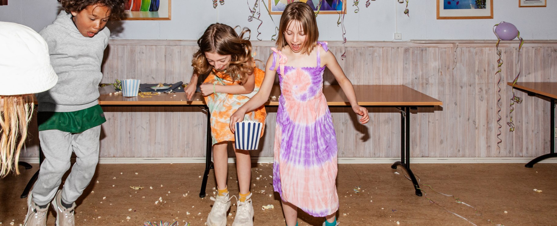 Tre barn leker i föreningslokal som är pyntad för kalas