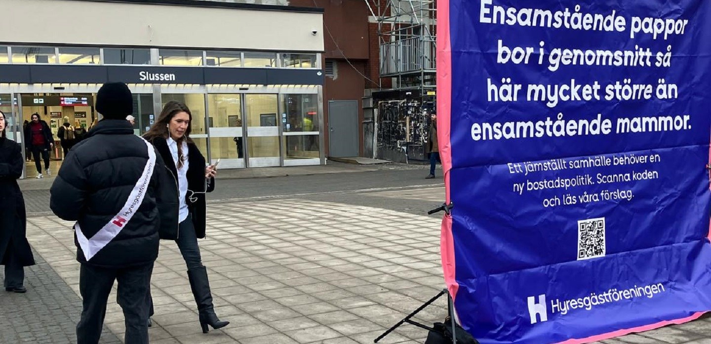 Personer på Slussen i Stockholm som går förbi blått plakat om jämställdhet