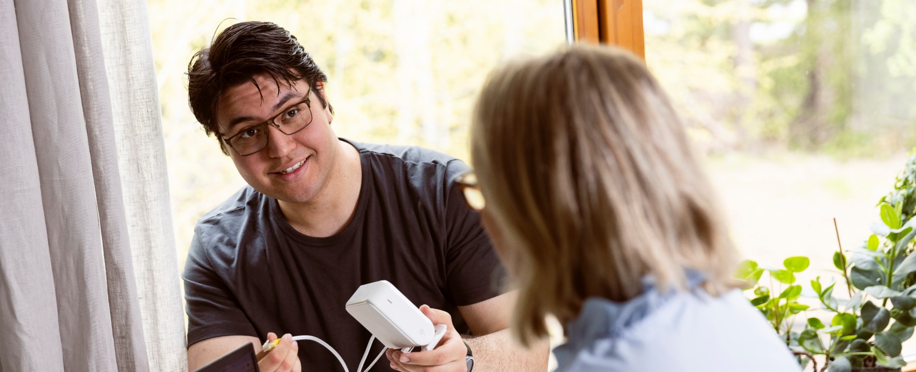 En Hemfixare sitter vid ett bord och hjälper en kvinna med teknik i hemmet
