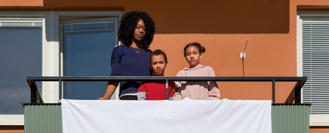 En mamma med 2 barn står på en balkong med banderollen Stoppa bo-orättvisan