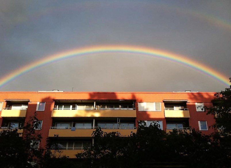 Regnbåge på grå himmel över bostadshus