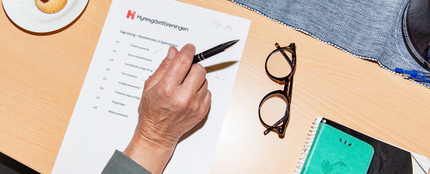 Äldre hand med penna och protokoll, kaka vid sidan om