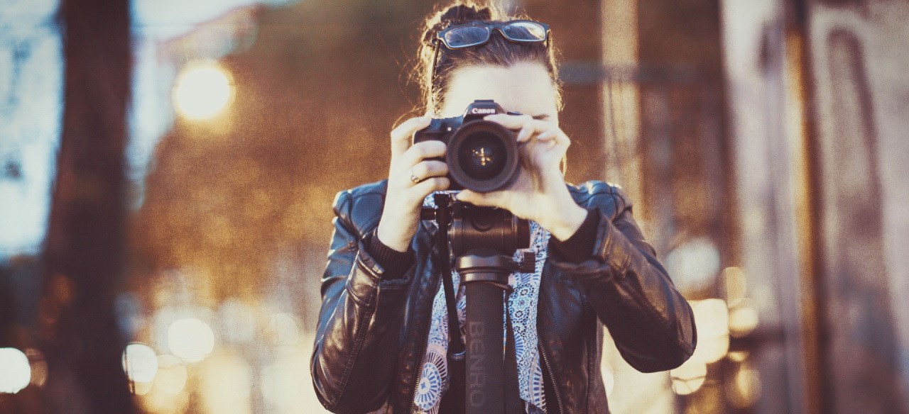 Foto framifrån av ljushyad kvinna med kamera framför ansiktet.