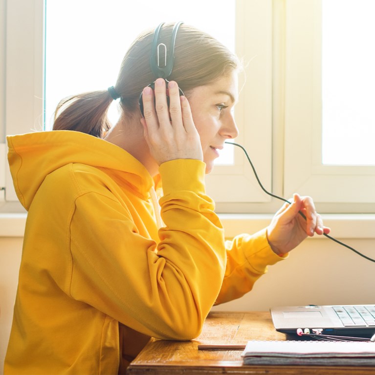 Ung kvinna klädd i gult pratar i mikrofon framför laptop