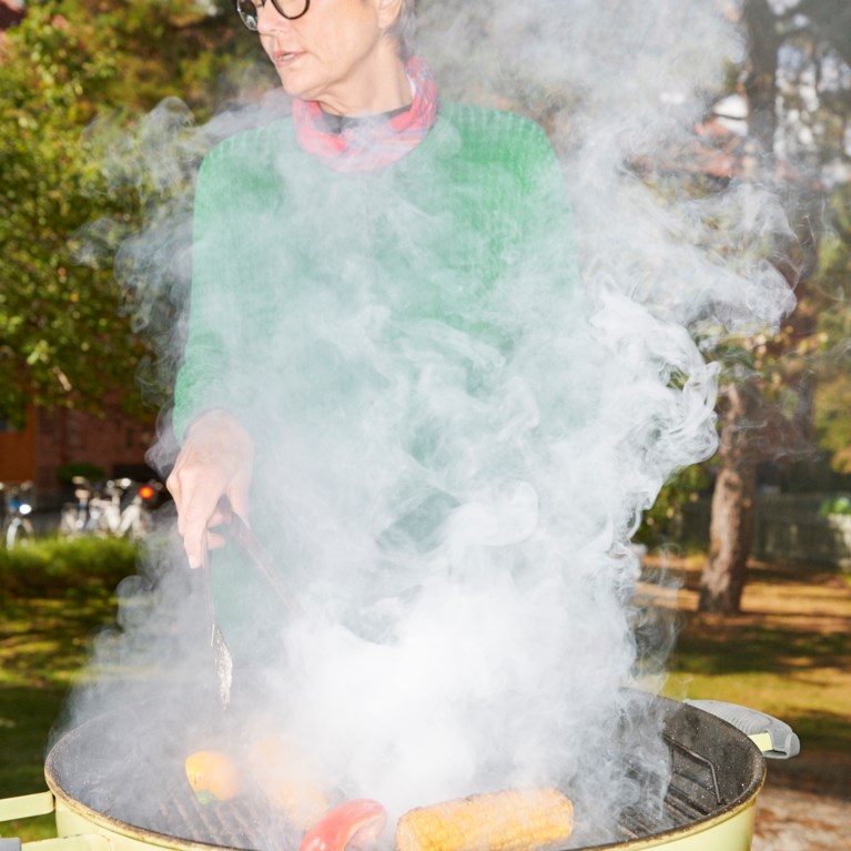 Kvinna står vid en grill som ryker utomhus på gården