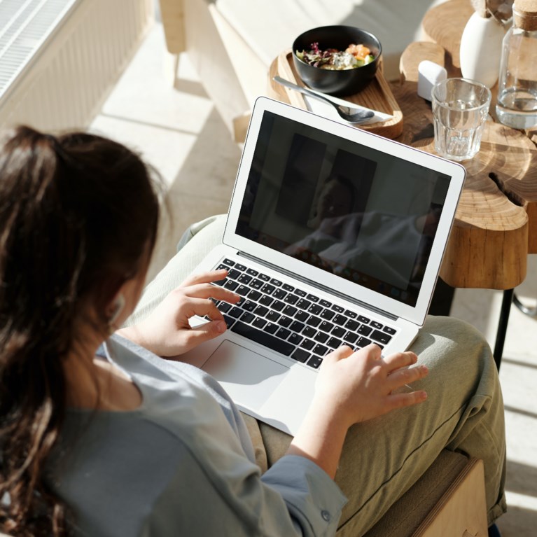 En kvinna sitter och jobbar med sin laptop i knät.