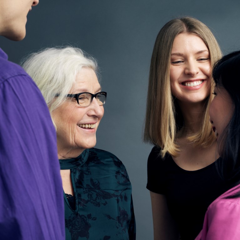 Fyra personer i olika åldrar som står och samtalar med varandra. Man ser en äldre kvinna framifrån.