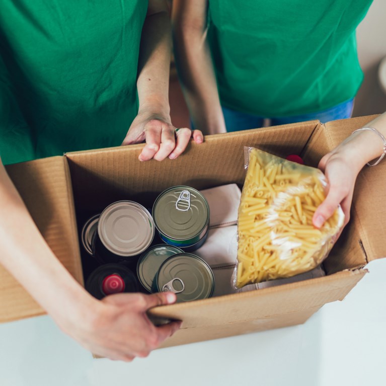 Händer som håller i en kartong med konservburkar, pasta och mat som håller länge.
