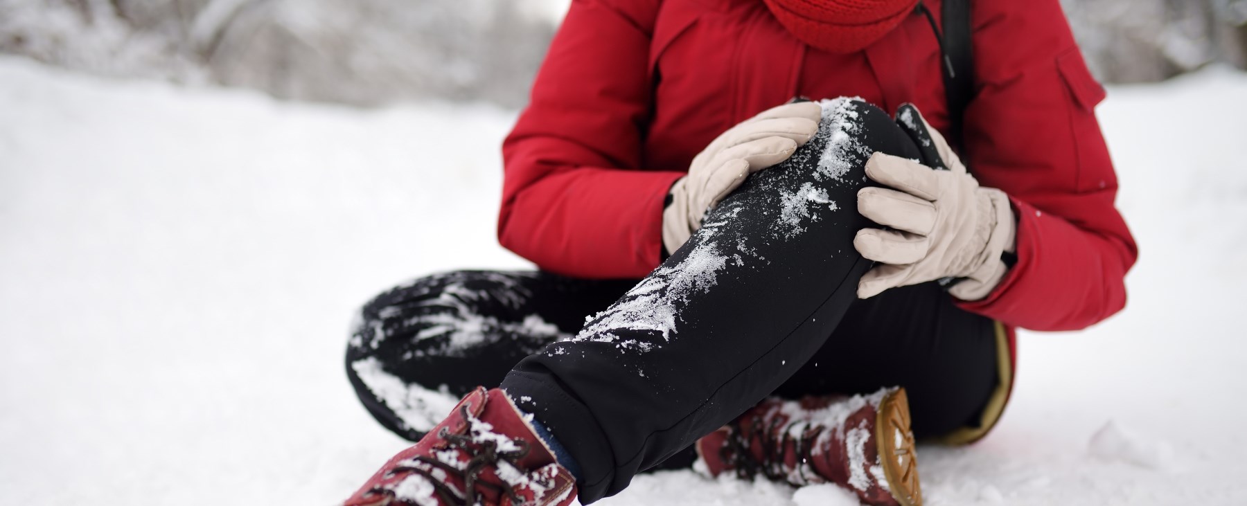 Kvinna har ramlat sitter i snö och håller sig för knät.