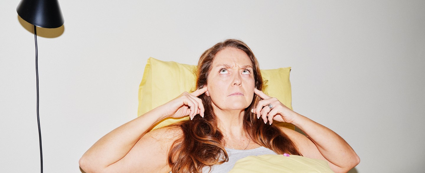 Kvinna sitter i sängen och håller för sina öron