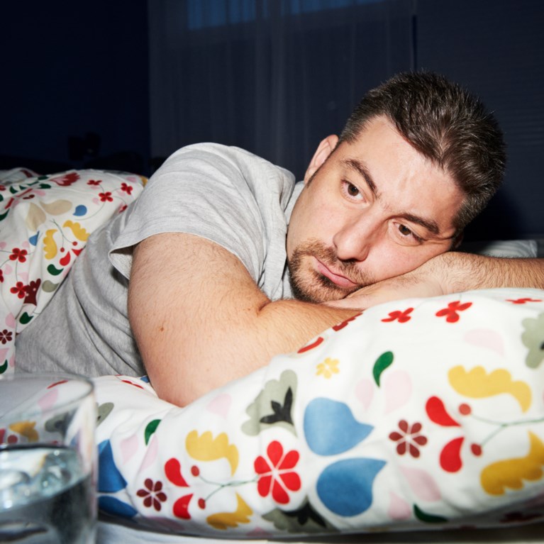 En man ligger i sängen, ser trött ut