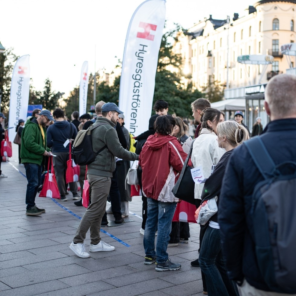 Människor står i kö på ett torg.