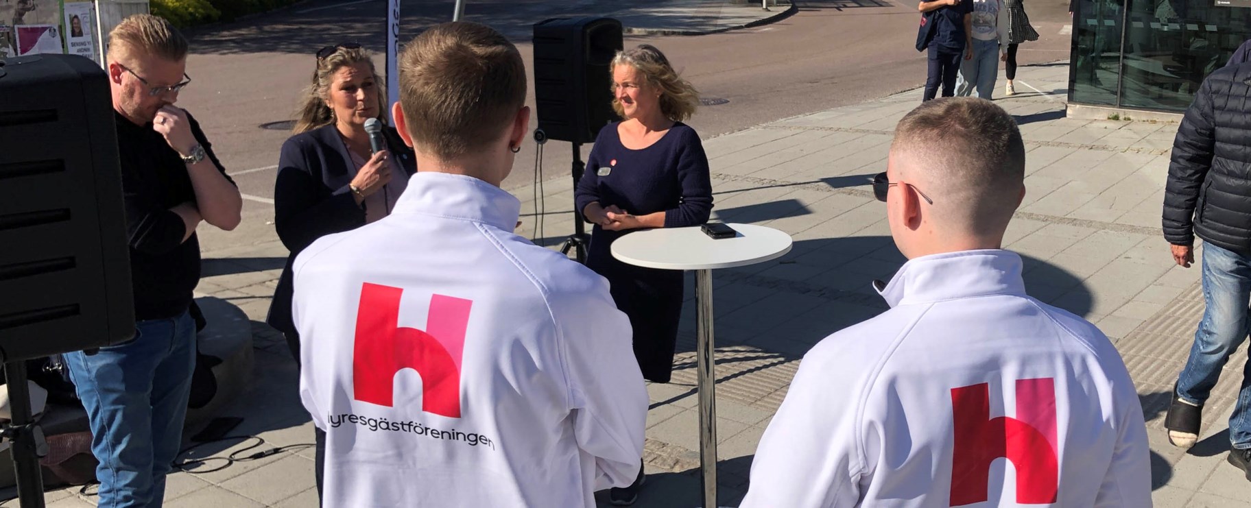 Sigge och Melvin står med ryggen mot kameran och tittar på politikerna som står bakom ett runt bord.