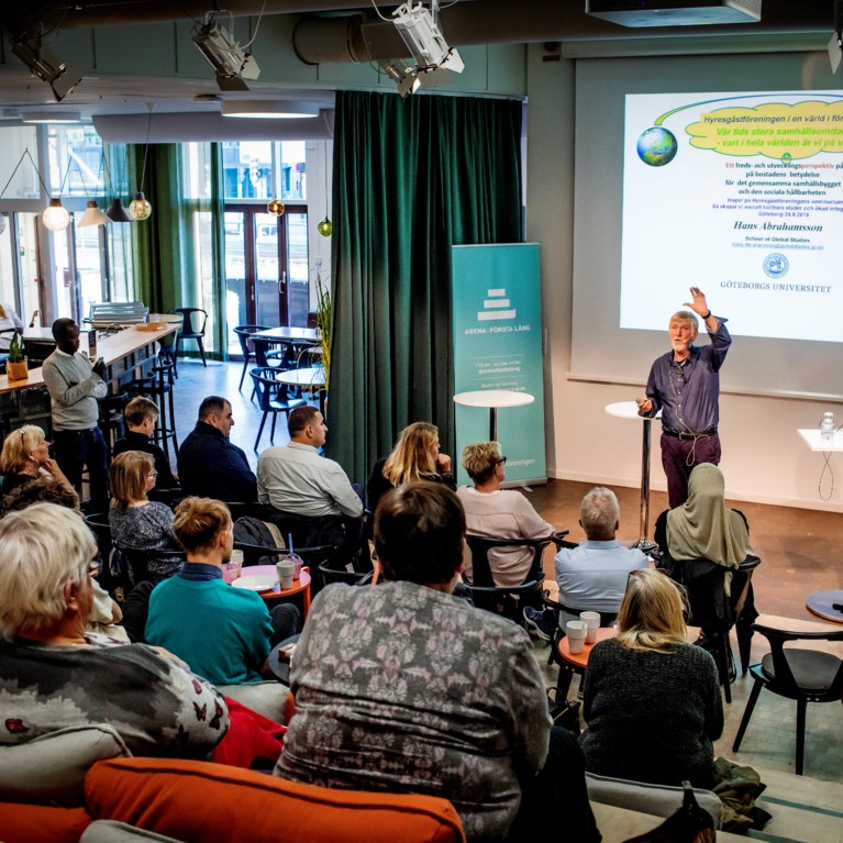 Foto från ett evenemang i vår Arena: Första Lång. Bilden är tagen från en läktare, i förgrunden ser man publik och som sitter vänd mot en föreläsare som står på scenen och pratar.