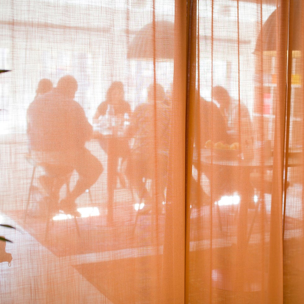 Bakom ett oranget skynke syns sju personer som sitter runt ett bord och samtalar