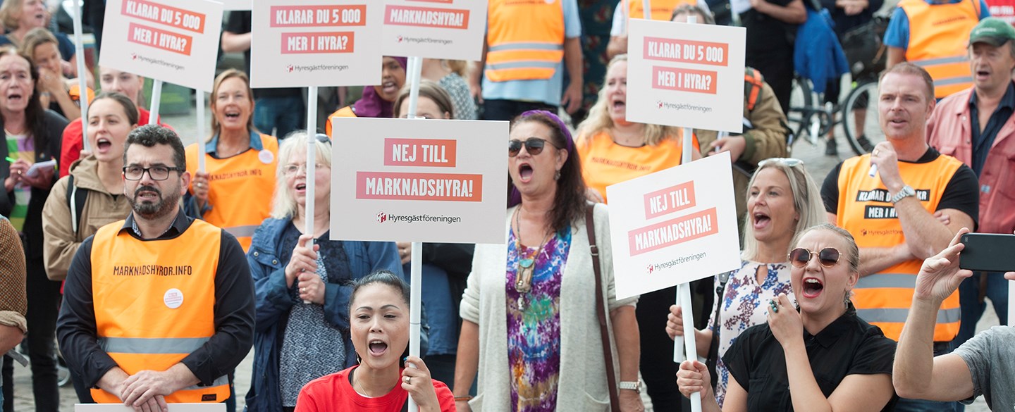 Foto på en folksamling med plakat där det står "Nej till marknadshyra"