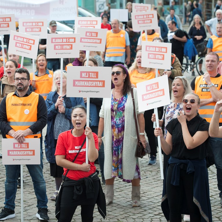 Foto på en folksamling med plakat där det står "Nej till marknadshyra"