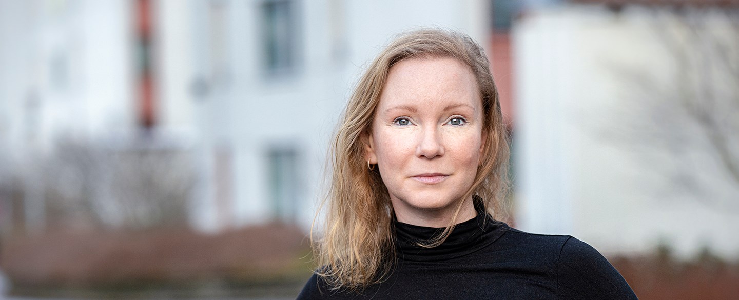 Bild på Sofi Bringsoniou som är förhandlare på Hyresgästföreningen region Västra Sverige när hon står framför ett bostadshus.