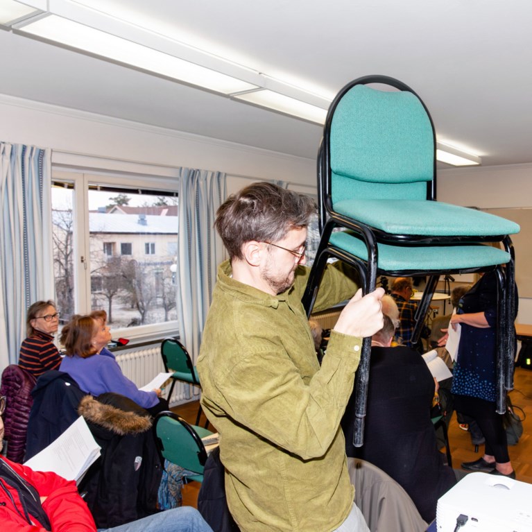 en man bär en stapel med stolar på ett möte