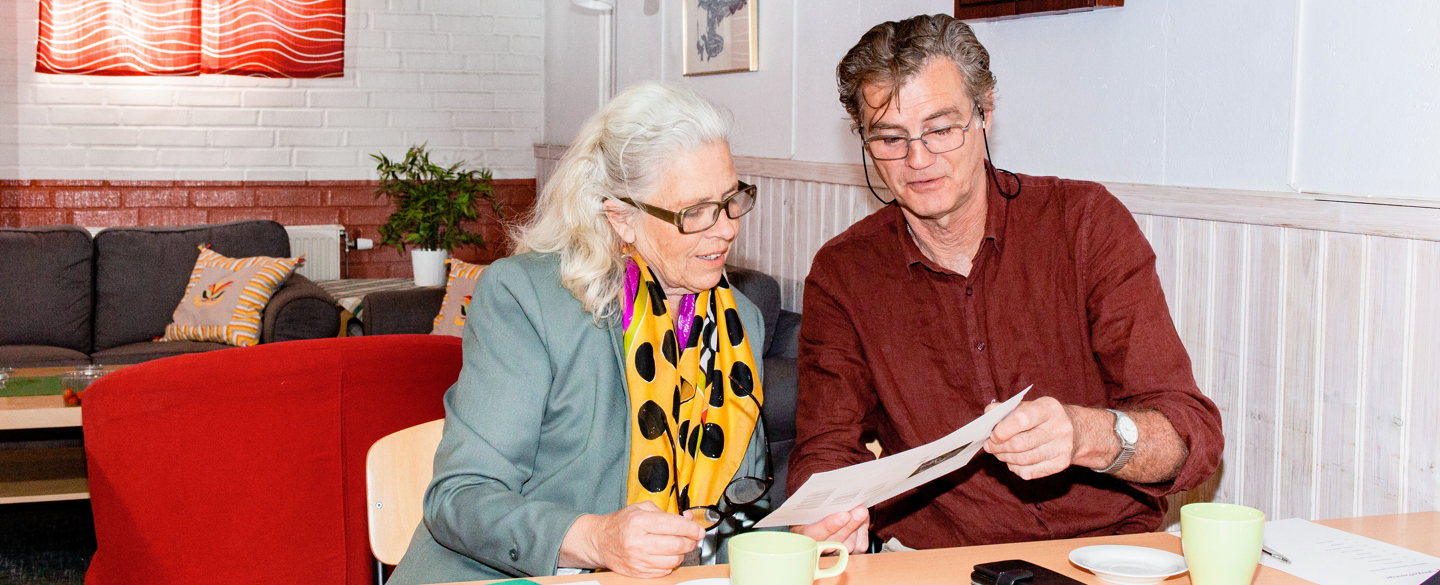 En man och en kvinna sitter vid ett bord och läser på ett papper.