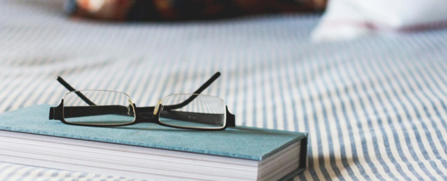En bok med läsglasögon på en säng