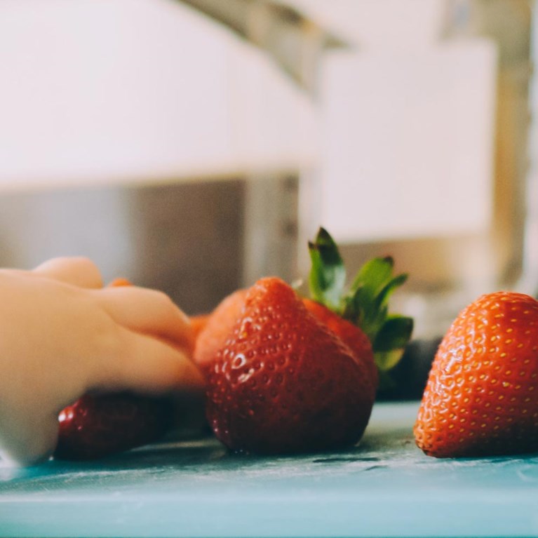 En barnhand tar en jordgubbe från ett fat