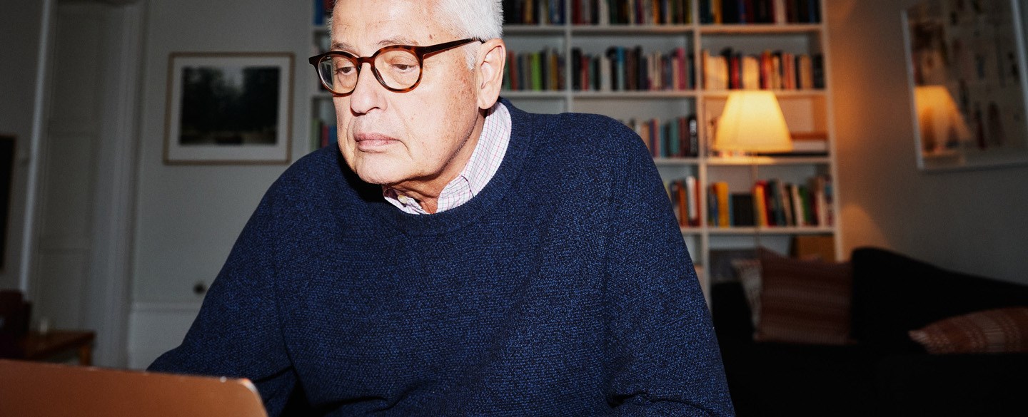 En äldre man i glasögon sitter framför en dator