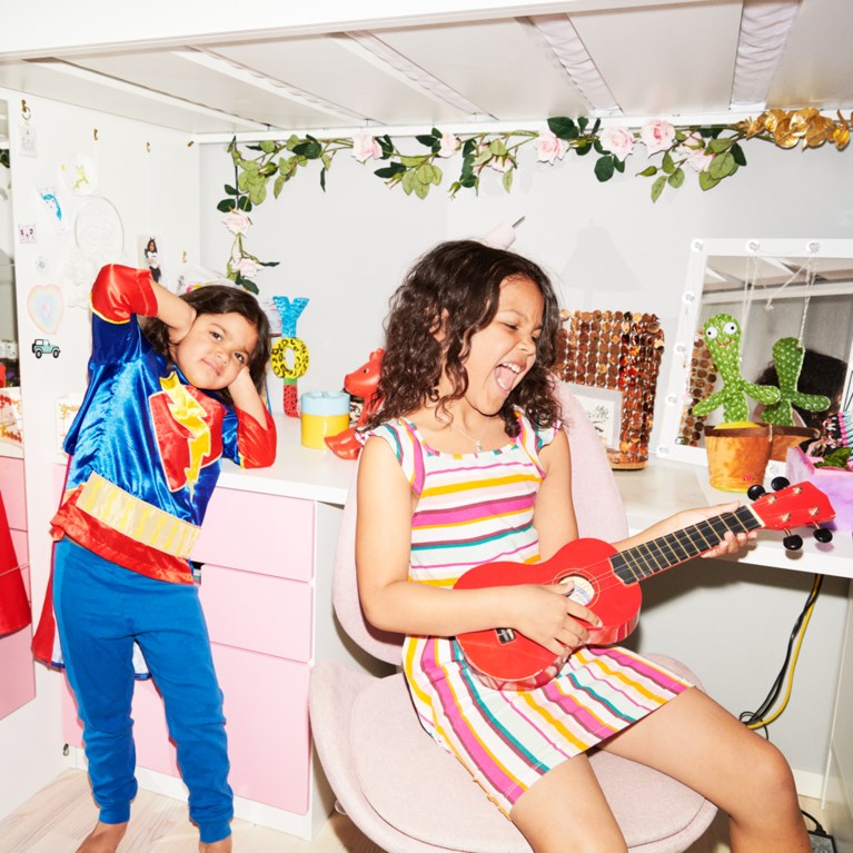 Ett barn spelar på en ukulele och ett barn håller för öronen