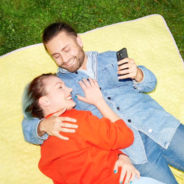 En man och en kvinna ligger på en filt på gräset och håller om varandra.
