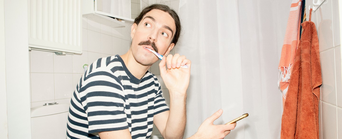 En ung man borstar tänderna i badrummet.