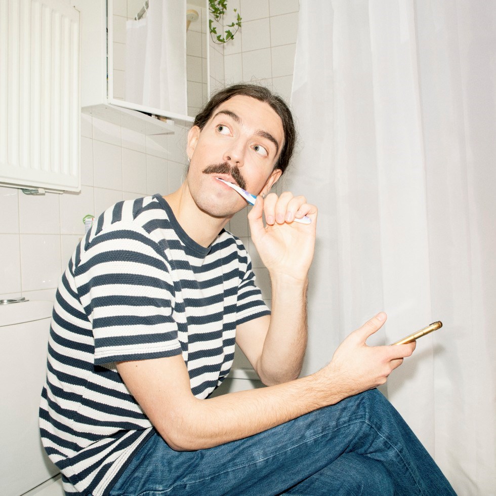 En ung man borstar tänderna i badrummet.