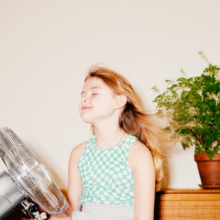 En flicka sitter framför en fläkt.