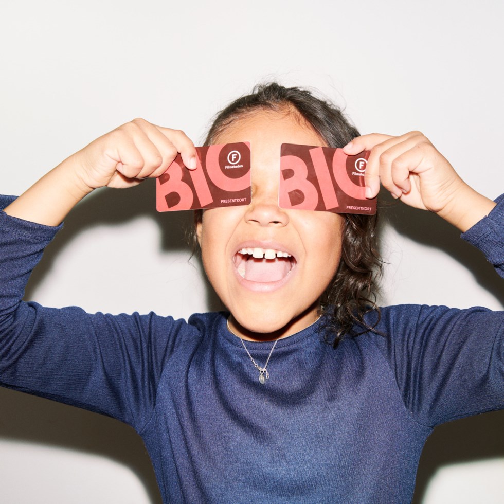 En flicka håller ett par biobiljetter framför sina ögon