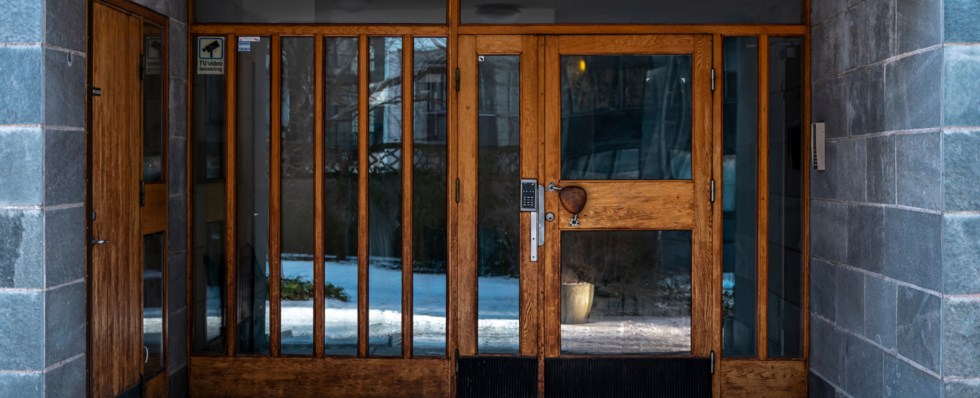 Portingång. Dörr- och fönsterglas med bruna lister av trä. Grå kakelväggar på sidorna.