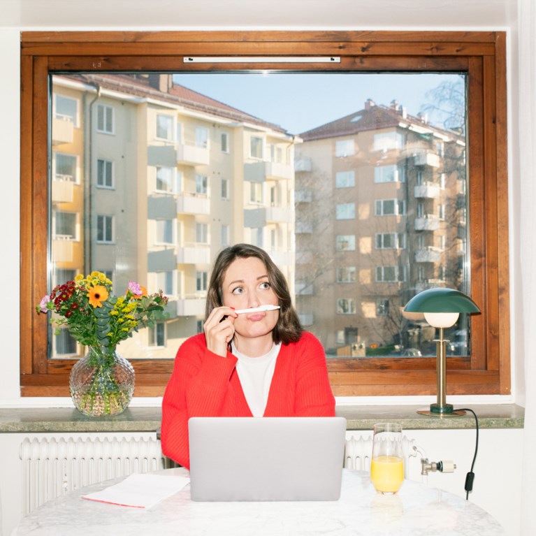 Kvinna sitter framför ett fönster och ser fundersam ut