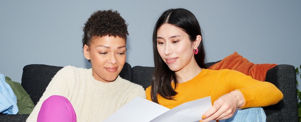 Två tjejer sitter på golvet och läser på två papper.