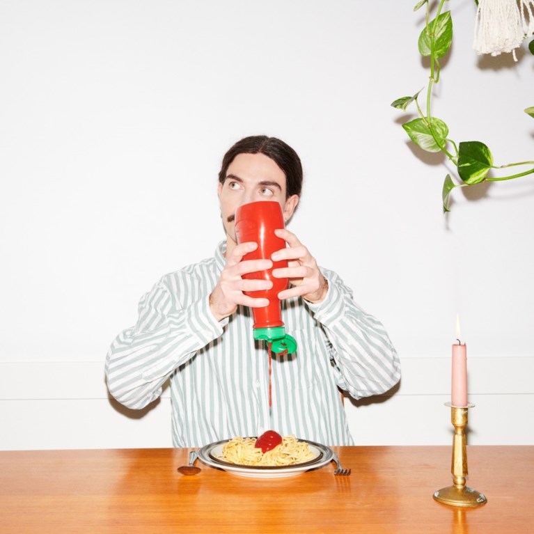En kille häller ketchup på en tallrik fylld med pasta