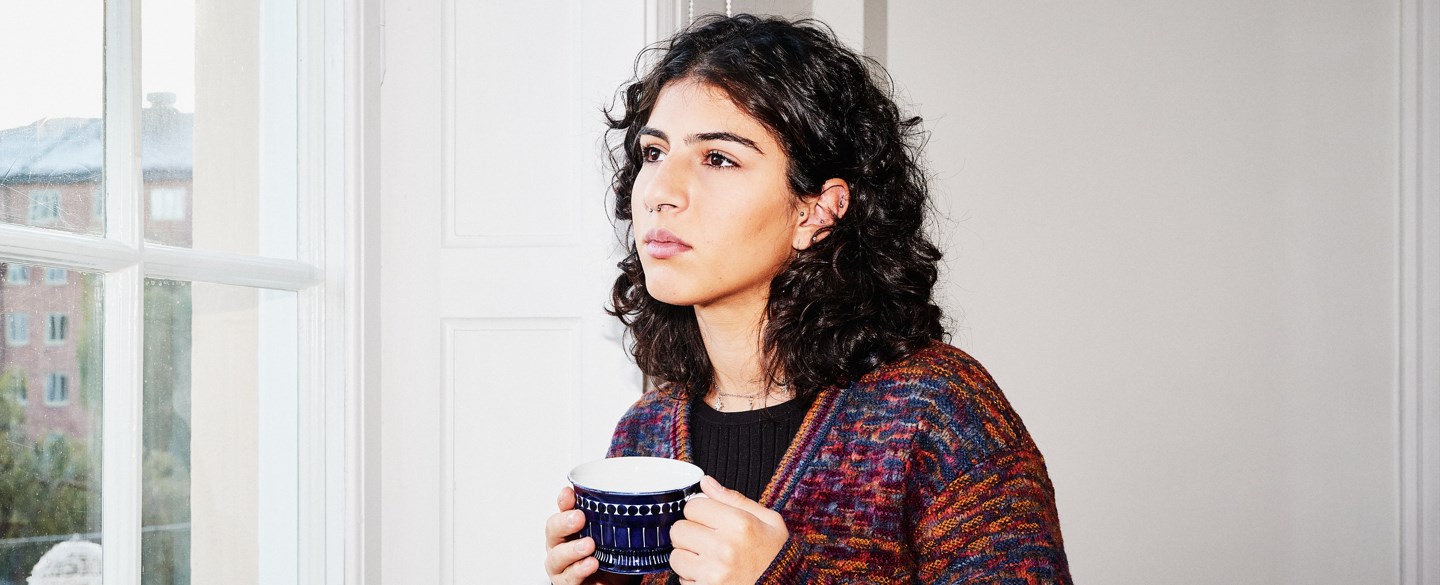 En ung kvinna blickar ut genom fönstret och håller i en kopp .