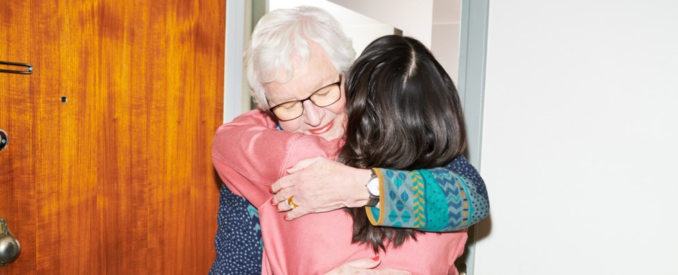 En äldre kvinna och en tjej kramas i en hall.